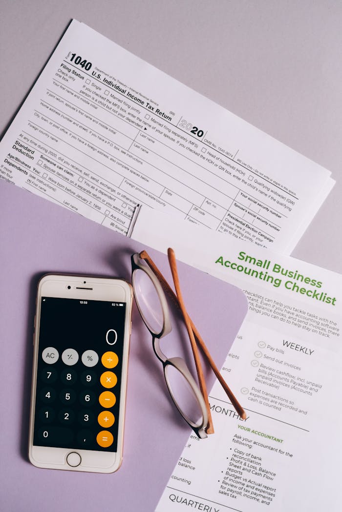 Flat lay of tax forms, checklist, smartphone, and glasses for small business accounting.